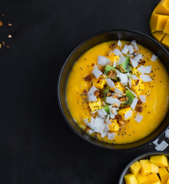 fresh mango and coconut smoothie bowl on black background, top view, square image