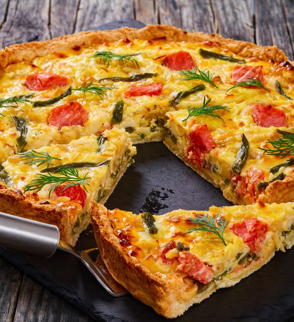 delicious french quiche with Salmon, green bean and Emmental cheese, cream, onion and eggs cut in slices on slate plate. piece of tart on spatula, view from above, close-up