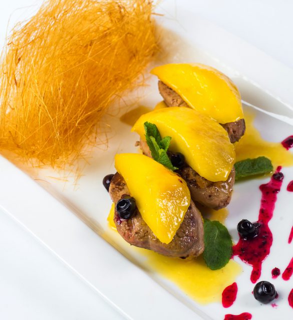 Pan seared foie gras on ripe mango and pomegranate reduction on white plate.