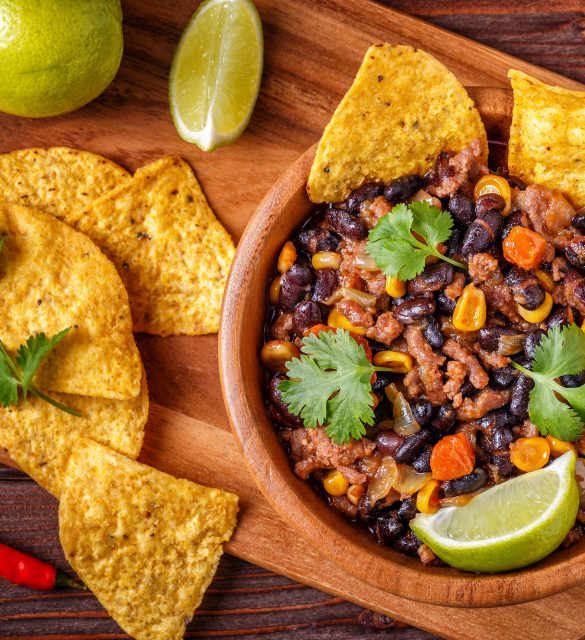 Chili con carne in bowl with tortilla chips on wooden background.