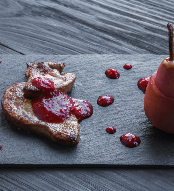 Creative french cuisine. Restaurant dish, seared foie gras served with berry sauce and pink pear on black slate plate. Delicatessen meal, roasted goose liver.